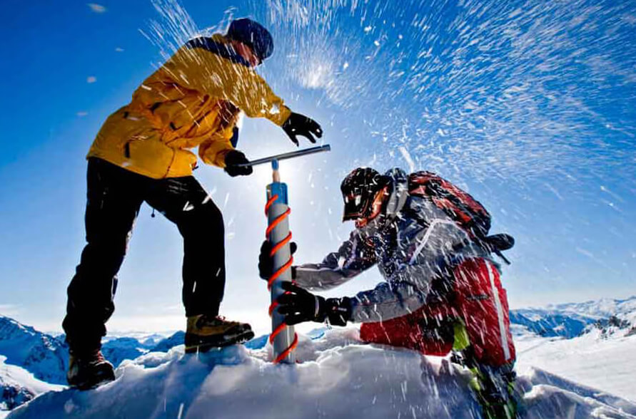 A photo of 2 researchers using a Kovacs ice coring drill to take ice samples